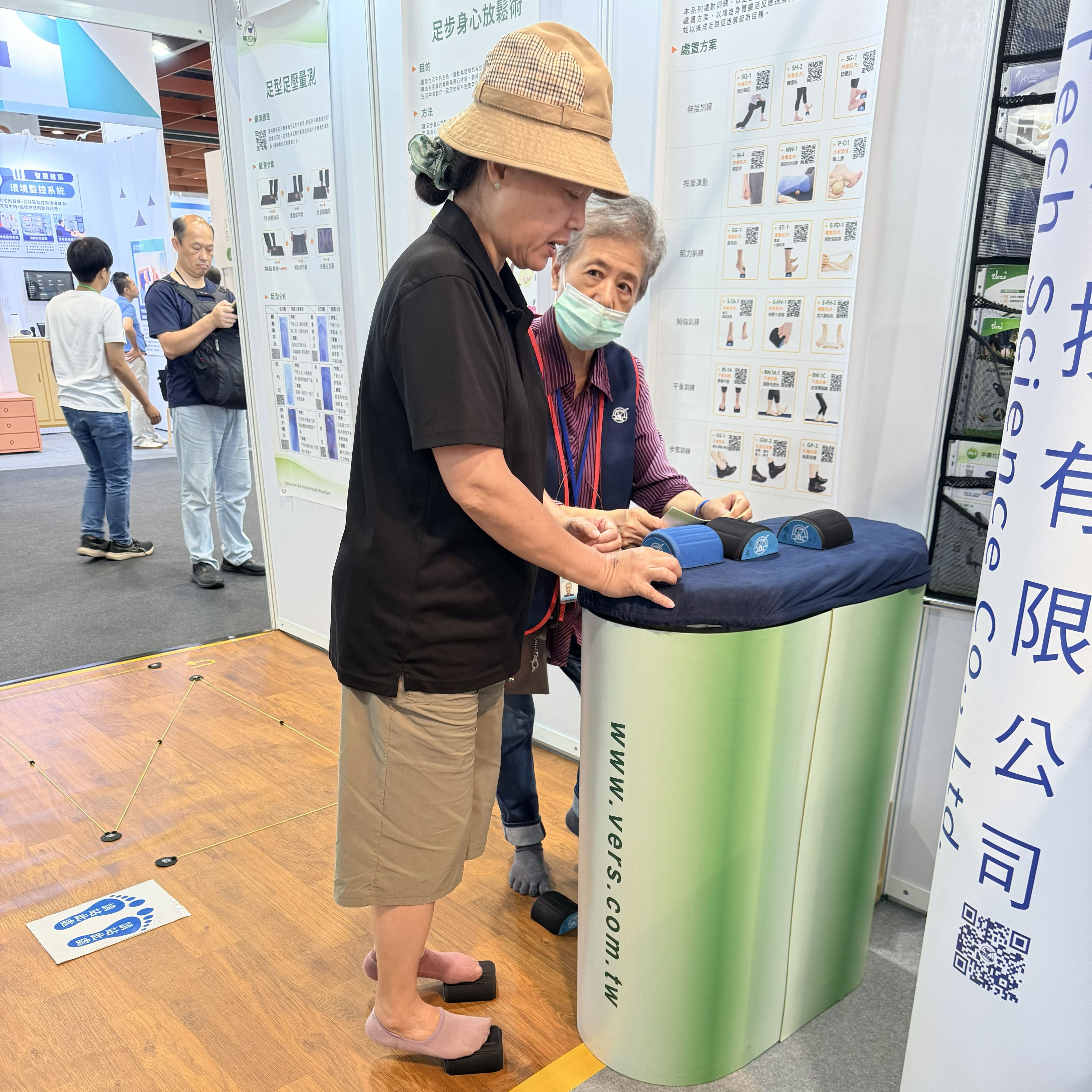 VERS博司科技展場人員一對一指導民眾體驗足部訓練輔具,進行靜態平衡與足趾受力覺察訓練